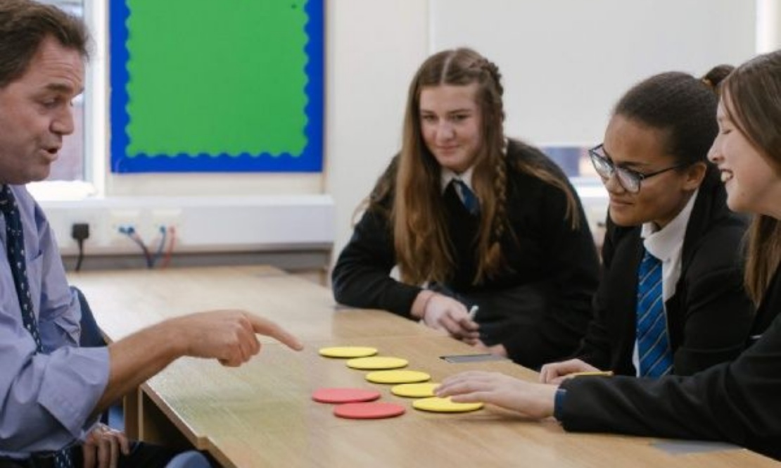A teacher pointing at counters with three pupils sat at a table